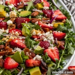 Strawberry arugula goat cheese salad on white serving plate topped with balsamic dressing.