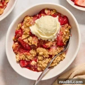 Strawberry crumble served in bowl with a scoop of ice cream and spoon scooping in.