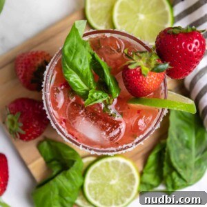 Overhead view of strawberry basil margarita with fresh lime and berries.