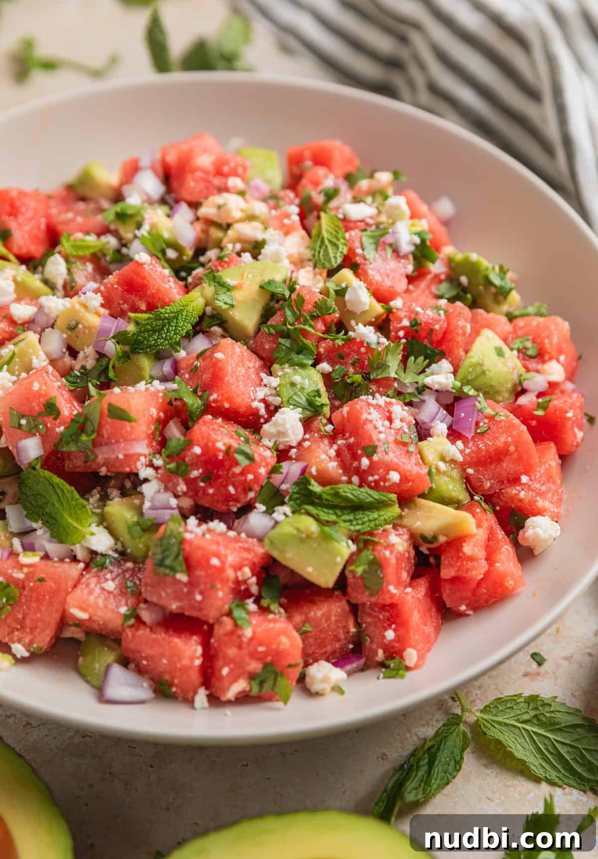 Watermelon and Avocado Salad with Feta and Mint 3 Watermelon salad with cubed avocado and feta in bowl topped with chopped cilantro and mint leaves.