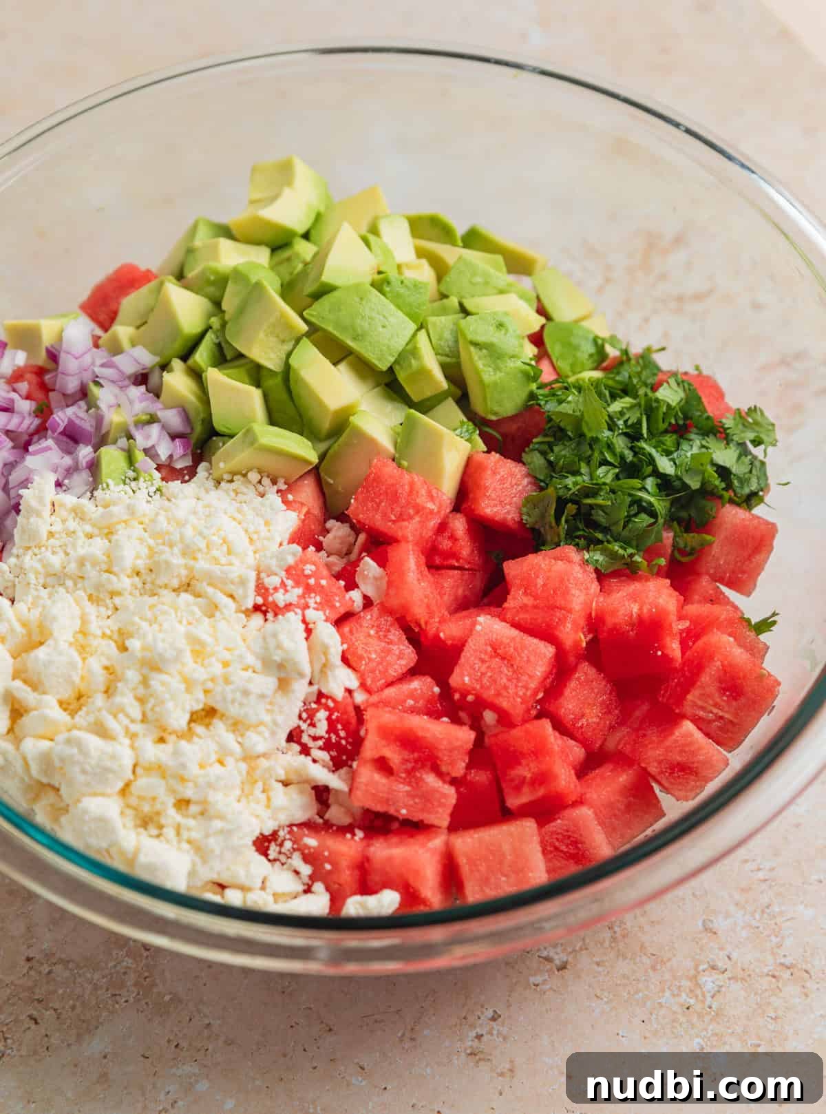 Watermelon and Avocado Salad with Feta and Mint 5 Diced avocado, feta cheese crumbles, cilantro, onion and watermelon cubes in glass bowl before mixing.