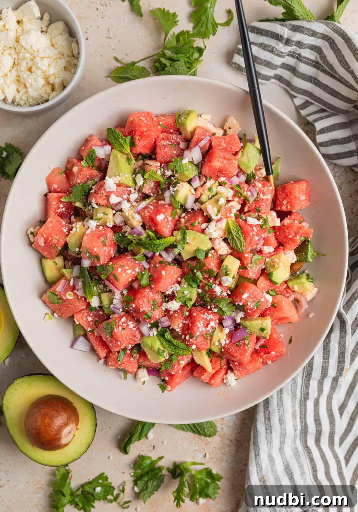 Watermelon and Avocado Salad with Feta and Mint 8 Overhead view of bowl with watermelon and feta salad with spoon and sliced avocado beside it.