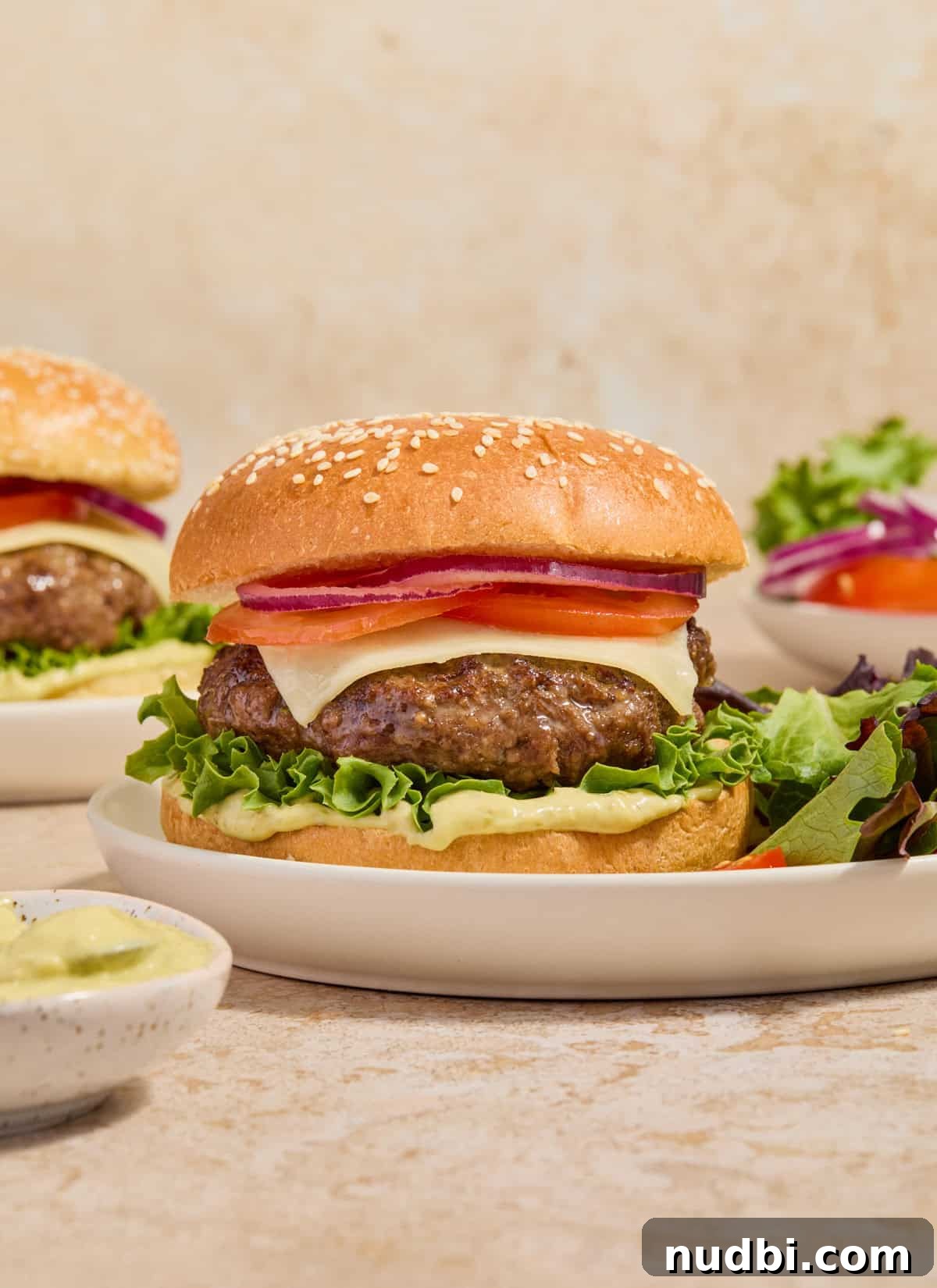 Juicy Mozzarella-Stuffed Burgers with Garlic Herb Buns 2 Stacked mozzarella burger on bun with pesto mayo, tomato, onion and greens.