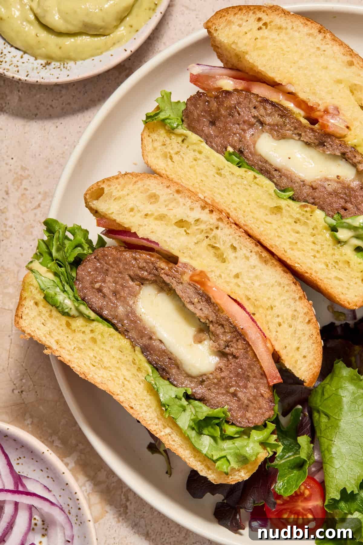 Juicy Mozzarella-Stuffed Burgers with Garlic Herb Buns 3 Mozzarella stuffed hamburgers cut in half on plate with salad.