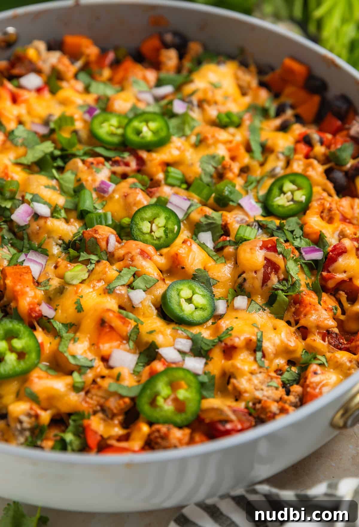 One-Pan Ground Turkey and Sweet Potato Skillet Recipe 3 Skillet with cooked meat and vegetables topped with melted cheese, cilantro, peppers, onions and more.