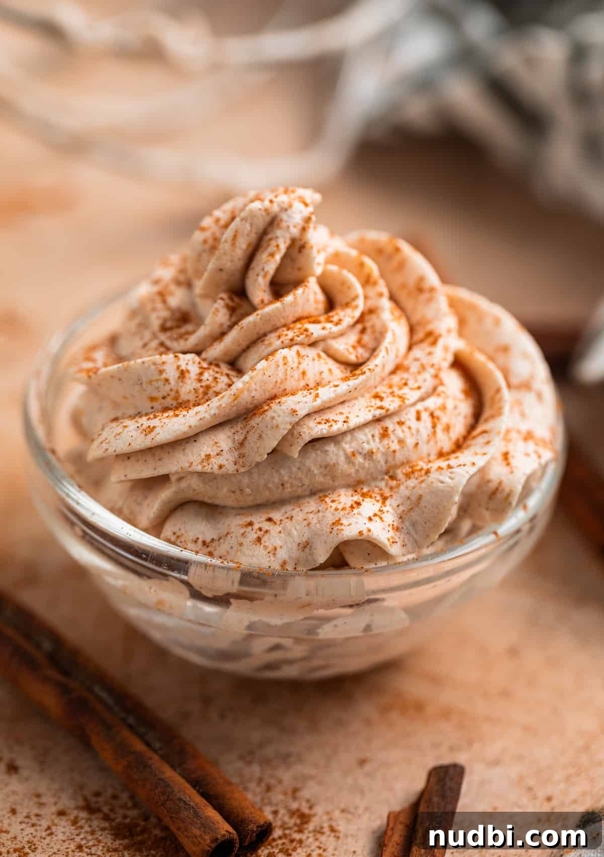 Pumpkin Spice Whipped Cream Recipe — Light & Fluffy Topping 2 Pumpkin spice whipped cream piped into glass bowl with cinnamon dusted on top and cinnamon sticks beside it.