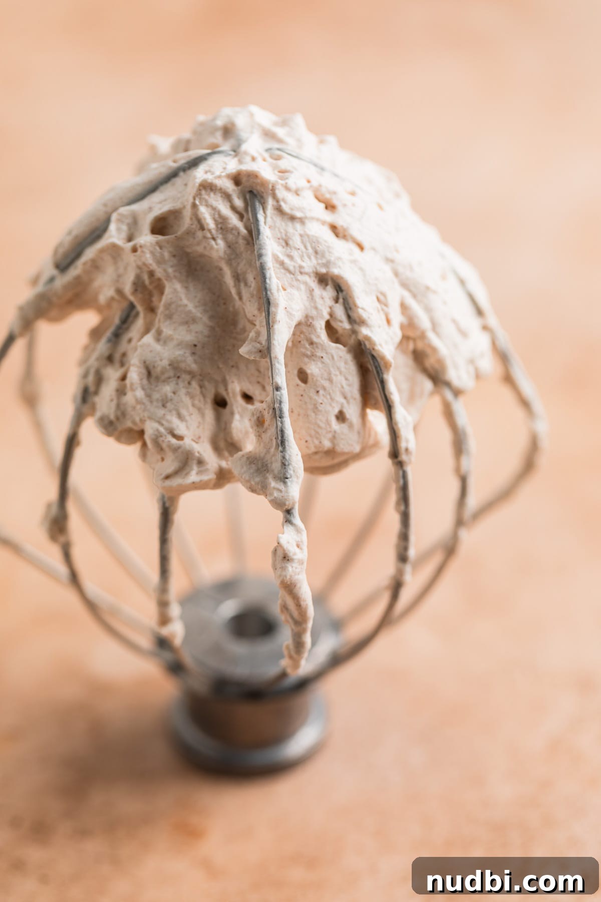 Pumpkin Spice Whipped Cream Recipe — Light & Fluffy Topping 3 Wire whisk from standing mixer with whipped cream on it.