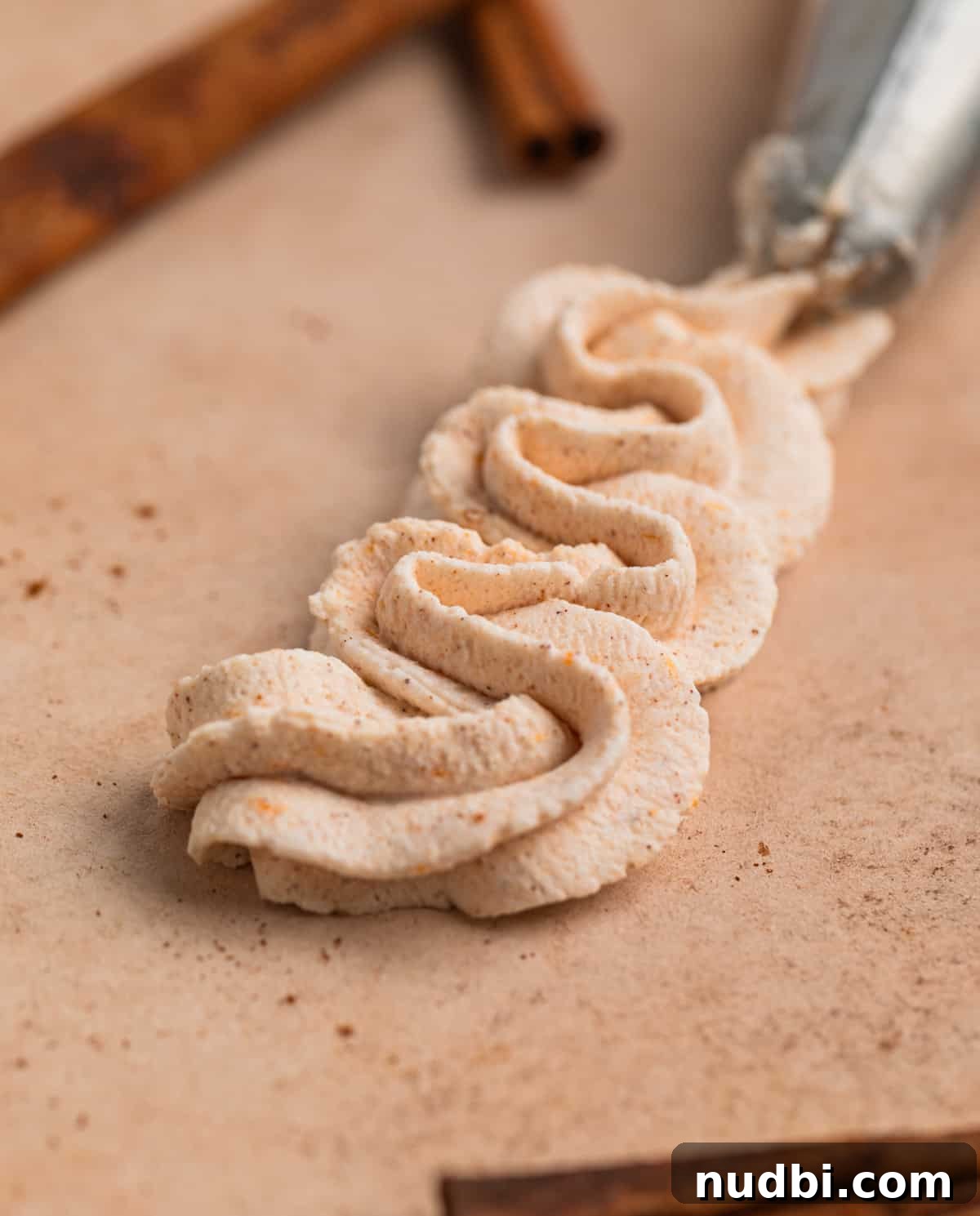 Pumpkin Spice Whipped Cream Recipe — Light & Fluffy Topping 8 Piped whipped cream on board with cinnamon sticks surrounding.