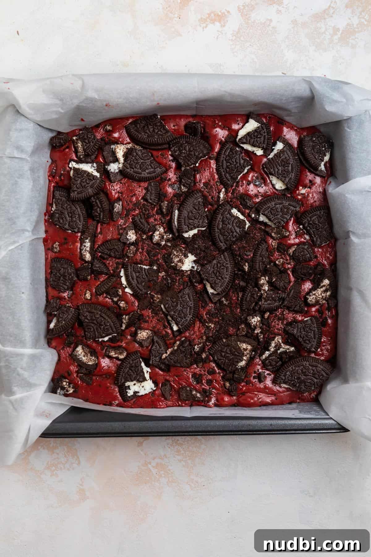 Decadent Red Velvet Oreo Fudge Recipe for Chocolate Lovers 7 Prepared fudge in parchment lined baking pan and topped with crushed up Oreos.