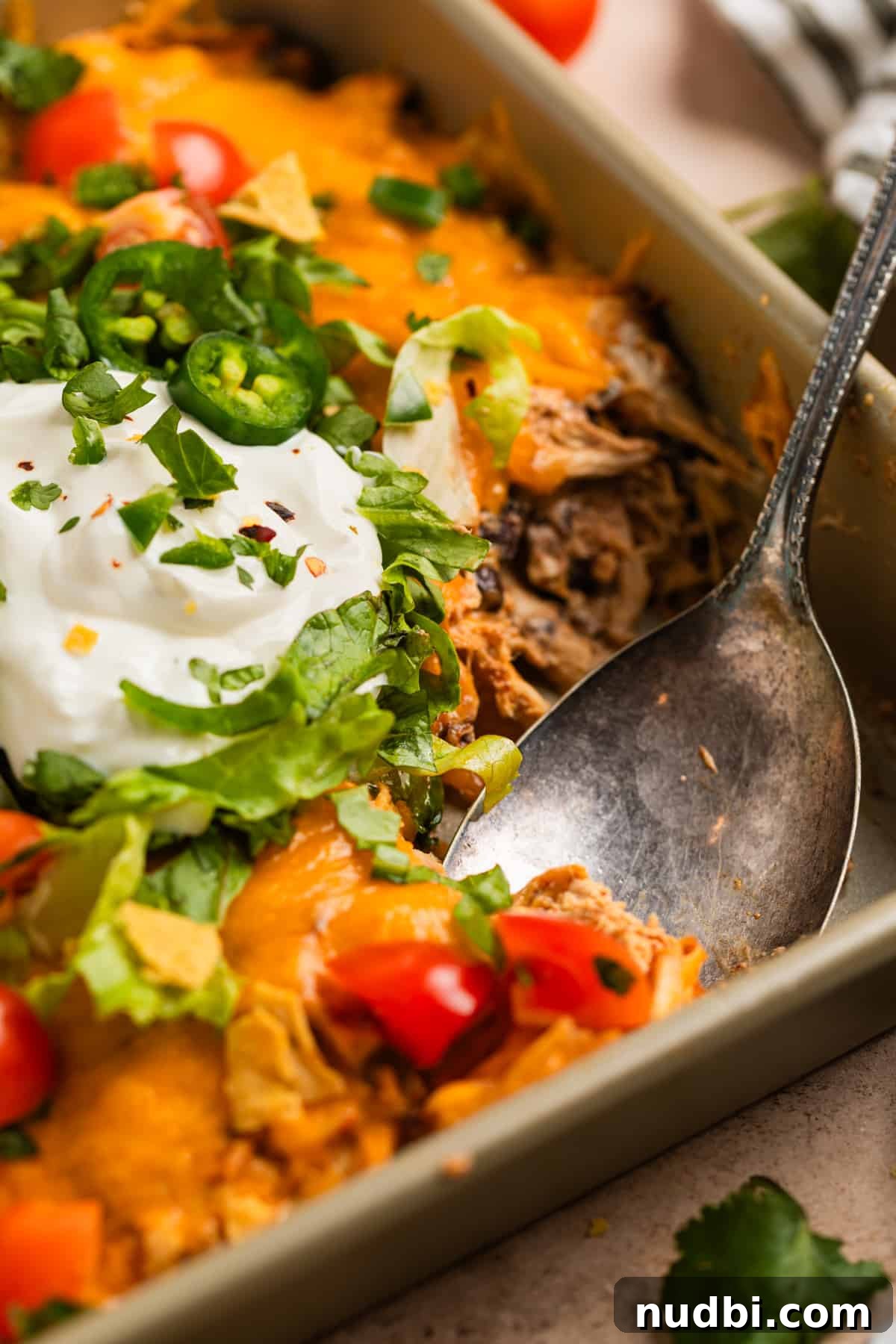 Cheesy Chicken Taco Casserole Bake with Crispy Tortilla Topping 3 Spoon scooping into pan with chicken casserole.