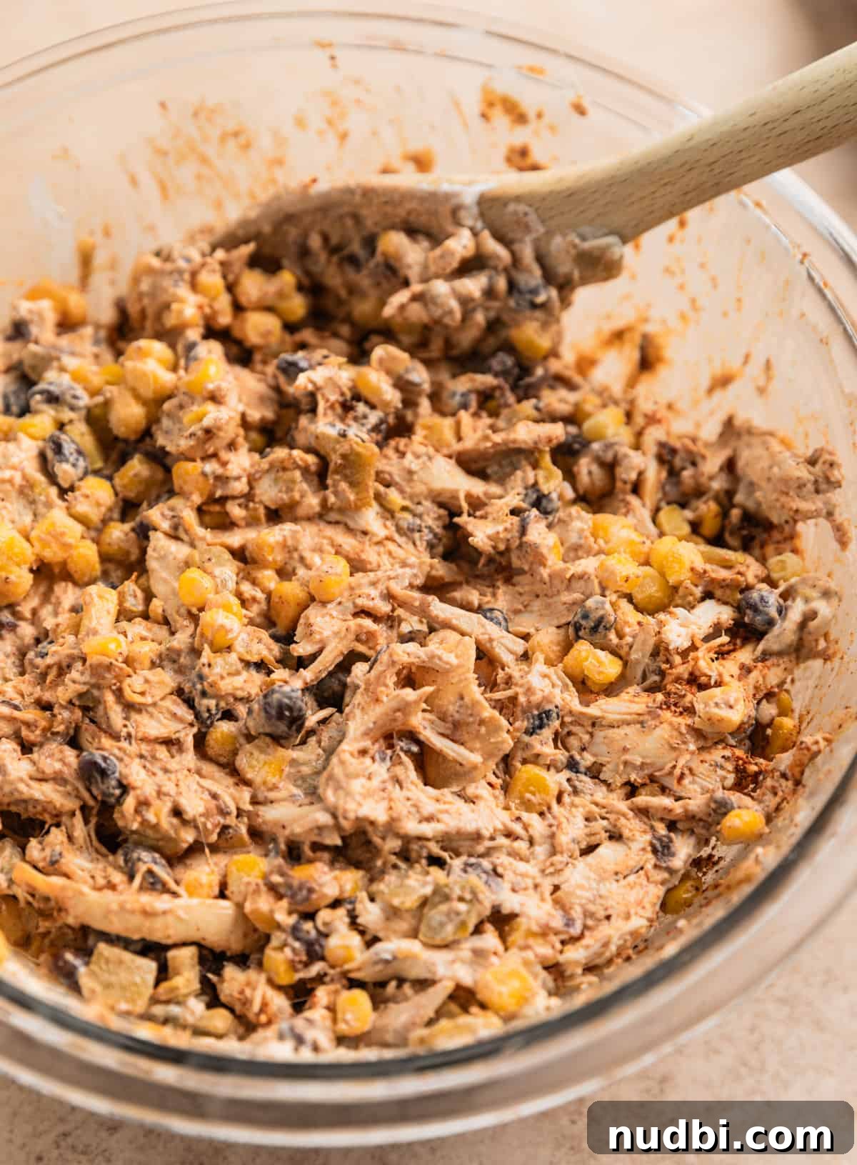 Cheesy Chicken Taco Casserole Bake with Crispy Tortilla Topping 4 Chicken, black beans, green chiles, corn and other ingredients in mixing bowl with spoon.