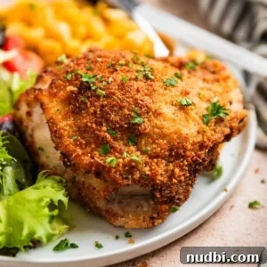 Crispy breaded air fryer parmesan chicken thigh on white plate topped with parsley.