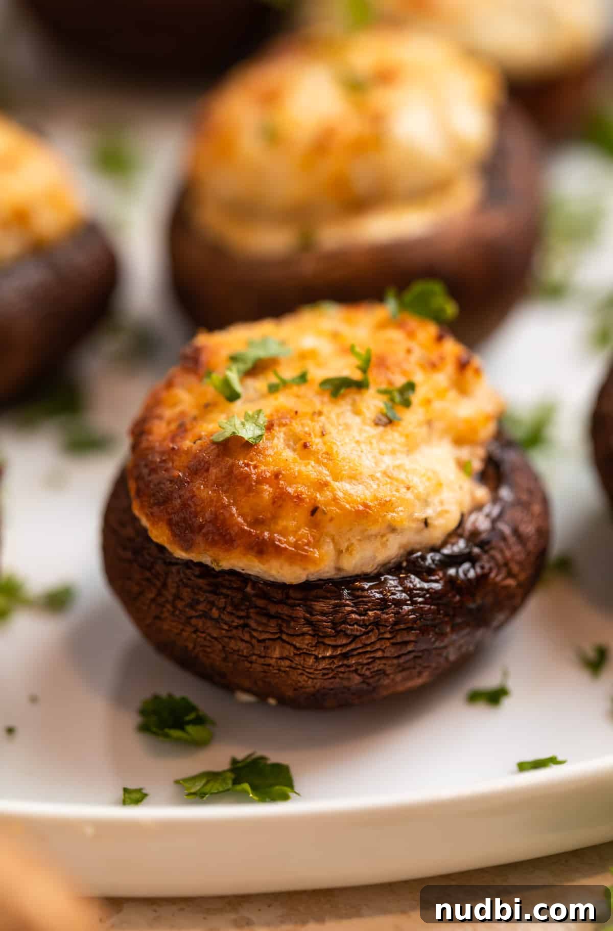 Crispy Air Fryer Stuffed Mushrooms Recipe for Quick Appetizers 2 Air fryer stuffed mushrooms on white plate topped with chopped parsley.