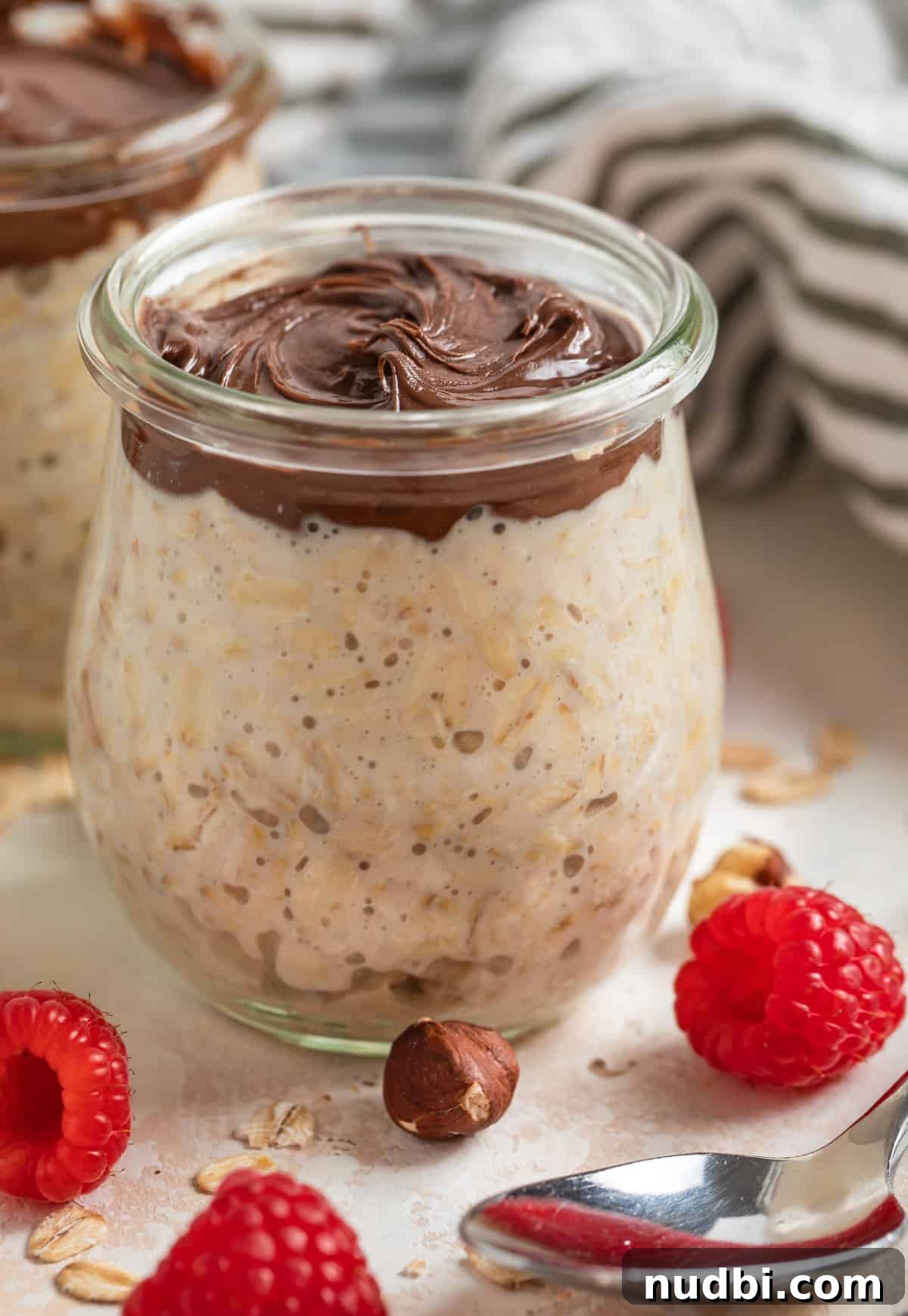 Creamy Nutella Overnight Oats Recipe for Quick Morning Meals 3 Nutella overnight oats in weck jar with berries and hazelnuts scattered around the jar.