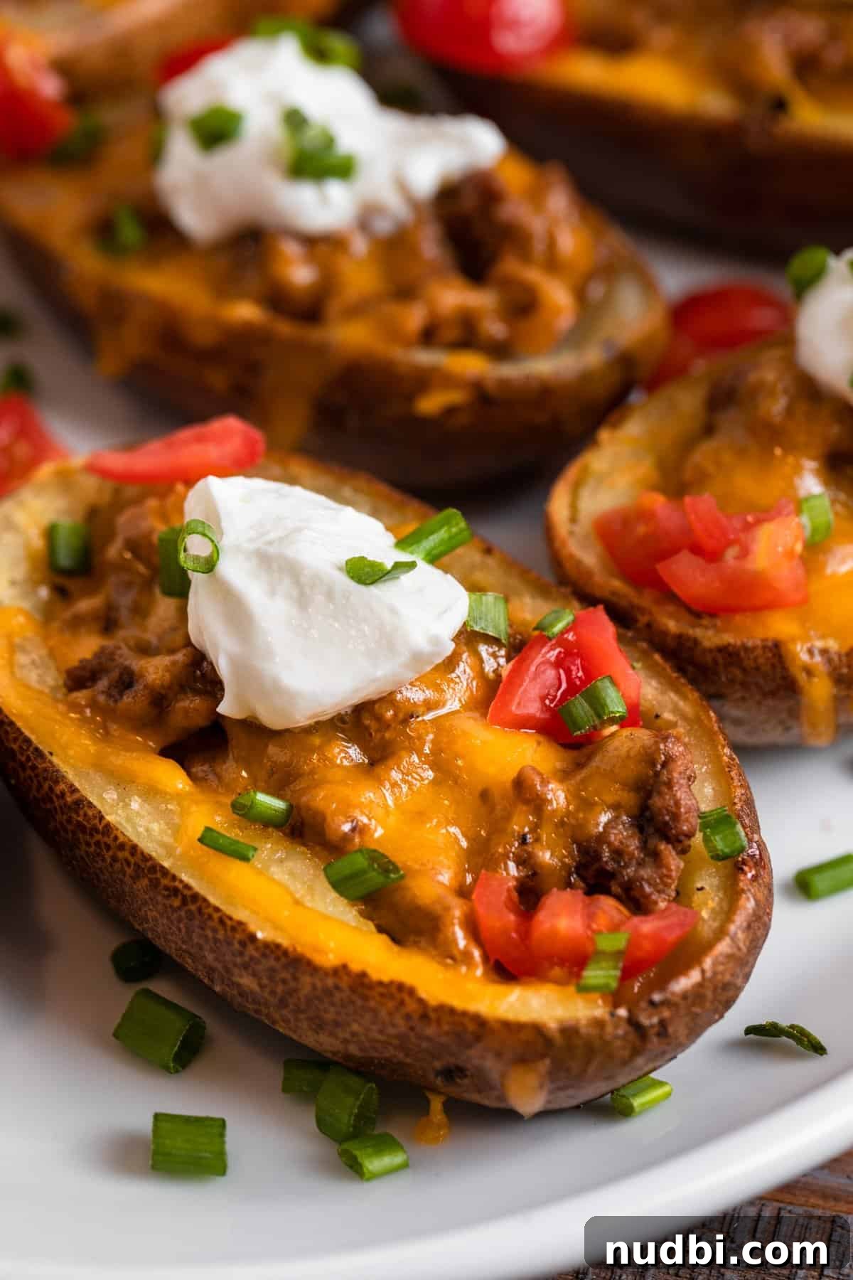 Cheeseburger-Stuffed Potato Skins: Loaded Appetizer Recipe 2 Cheeseburger stuffed potato skins on white plate topped with sour cream, chives and tomatoes.