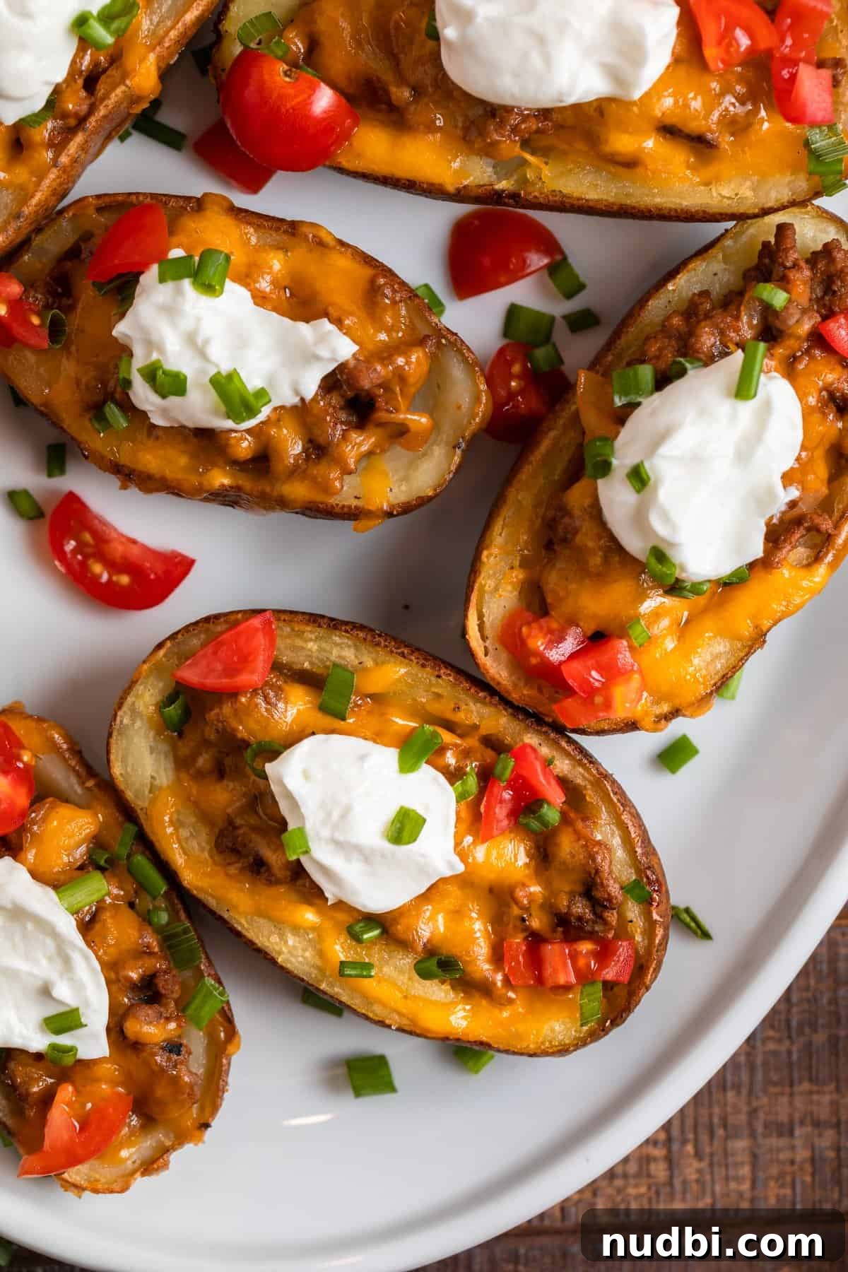 Cheeseburger-Stuffed Potato Skins: Loaded Appetizer Recipe 11 Cheeseburger stuffed potato skins on white serving dish with chopped tomatoes, chives and sour cream.