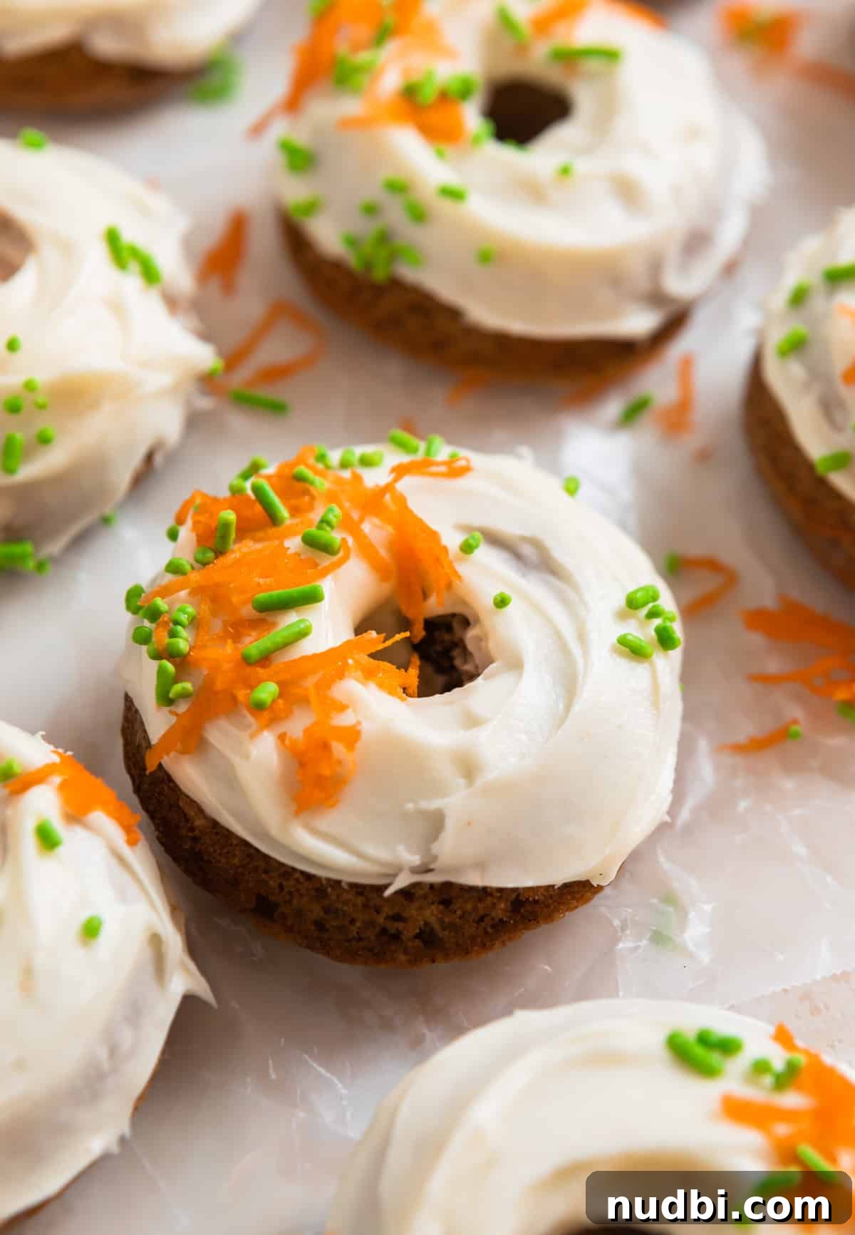 Carrot Cake Donuts with Cream Cheese Glaze: Moist Spiced Recipe 9 Carrot cake baked donuts with cream cheese frosting lined on parchment paper.