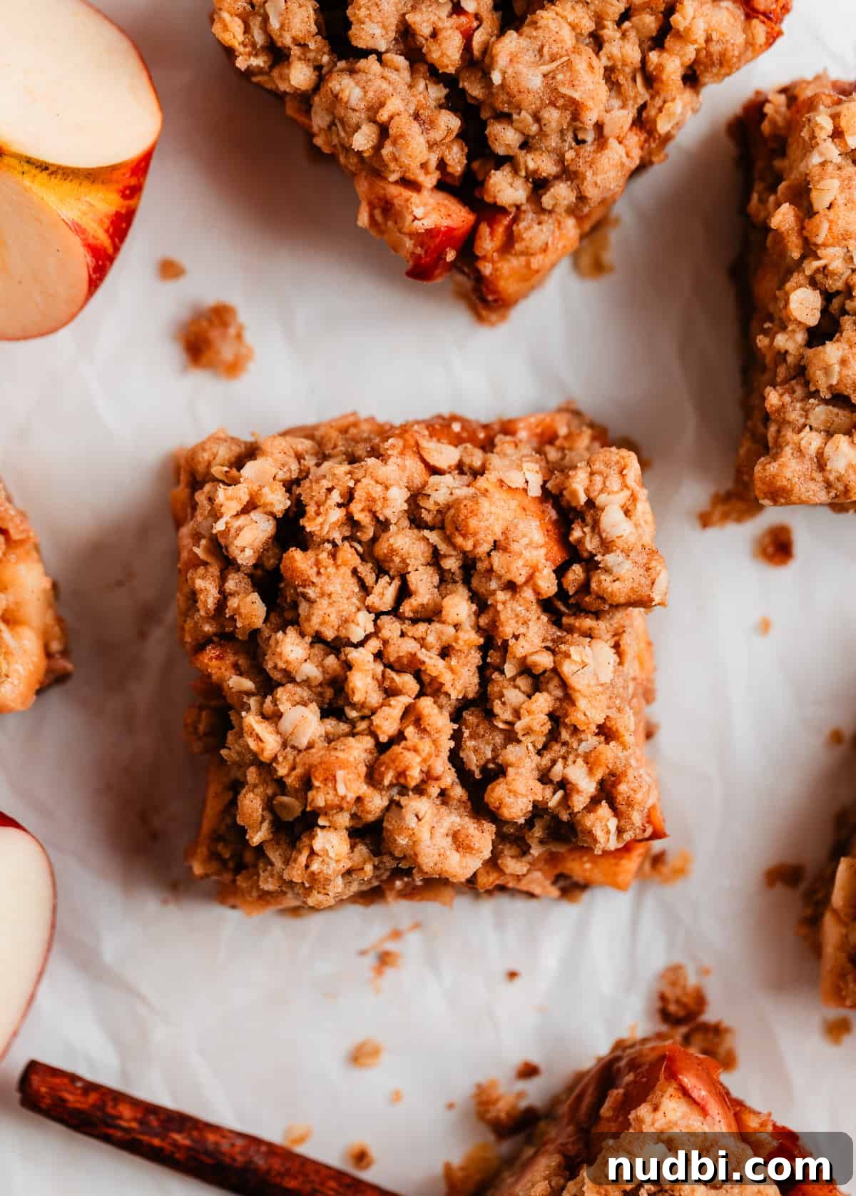 Homemade Apple Crumble Bars Recipe — Soft Filling & Crunchy Topping 7 Overhead view of apple crumb bar with cinnamon stick and sliced apple beside.