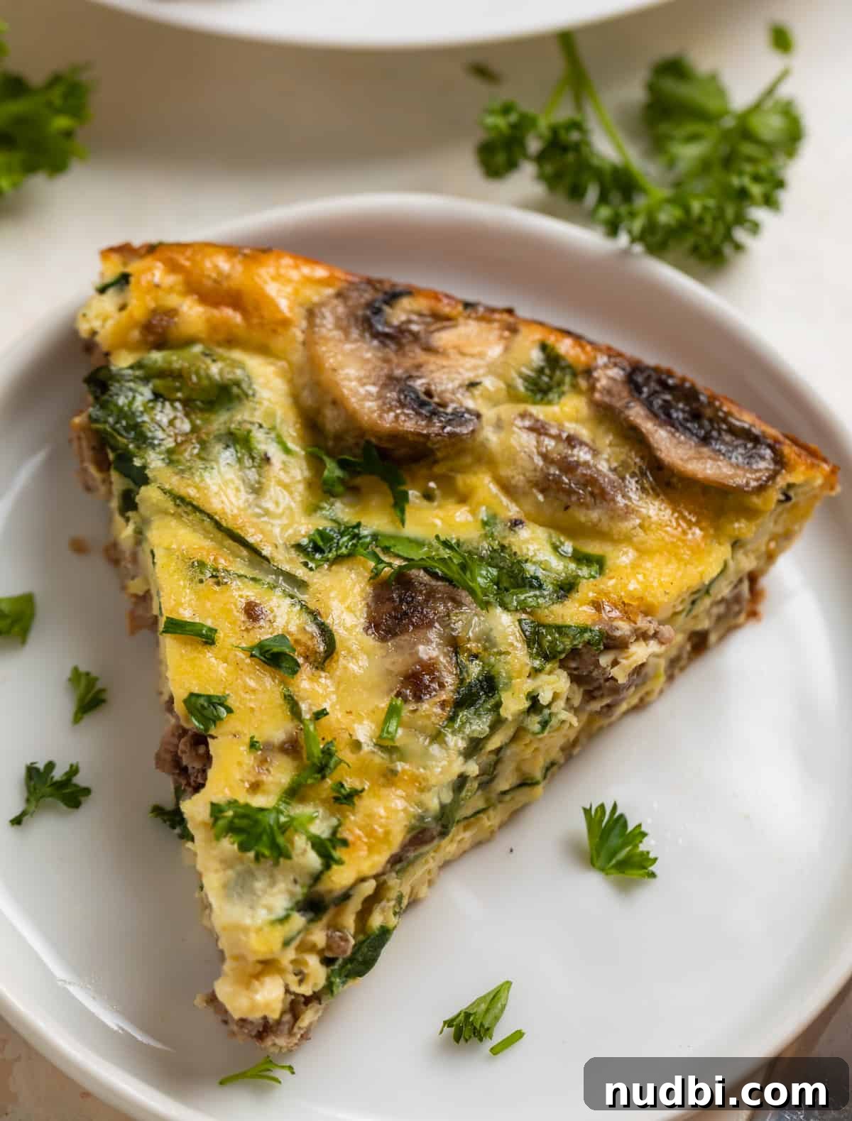 Savory Crustless Mushroom and Cheese Quiche Recipe 2 Crustless mushroom quiche with beef, swiss and spinach on white plate.