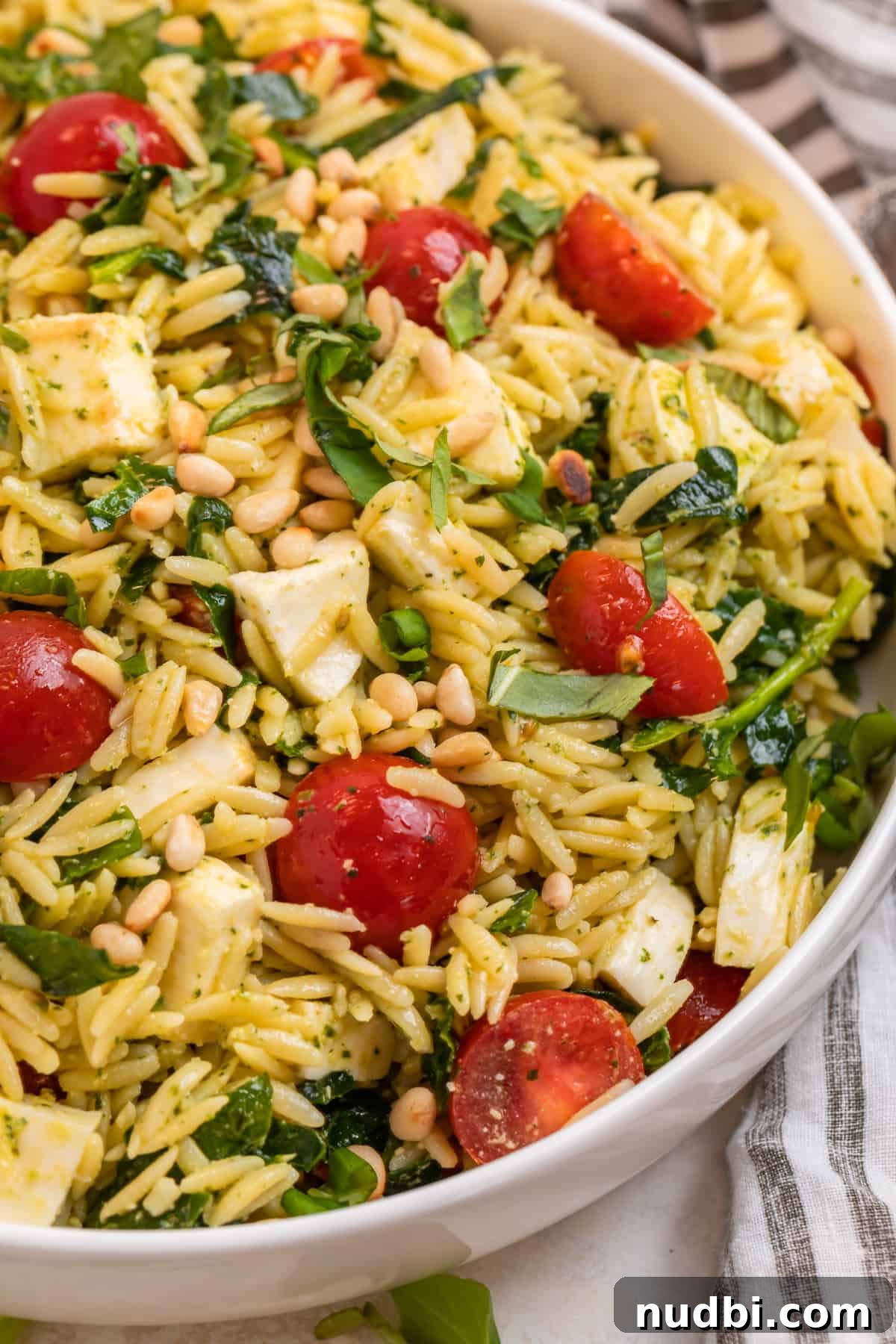 Creamy Pesto Orzo Salad with Cherry Tomatoes and Basil 2 Pesto orzo salad with cherry tomatoes, mozzarella and spinach in white bowl.