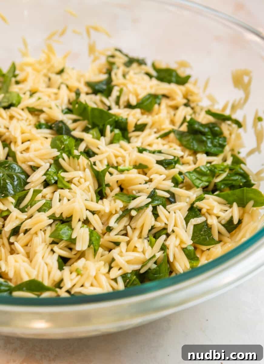 Creamy Pesto Orzo Salad with Cherry Tomatoes and Basil 7 Cooked orzo and spinach in glass mixing bowl