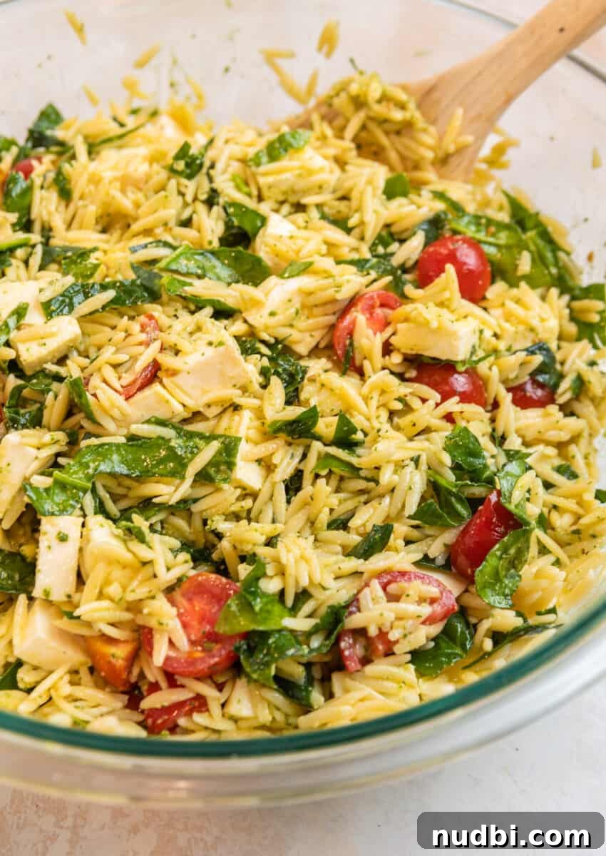 Creamy Pesto Orzo Salad with Cherry Tomatoes and Basil 9 Pesto orzo salad in mixing bowl with wood spoon.