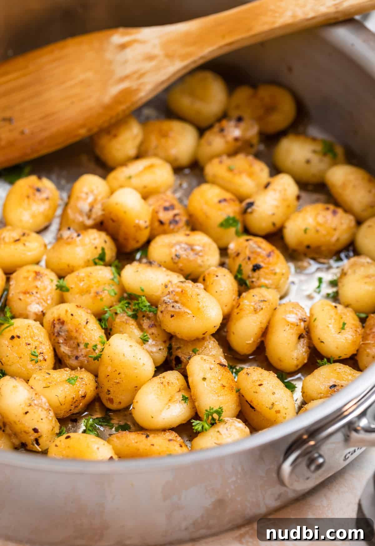 Crispy Pan-Fried Gnocchi with Garlic Butter and Parmesan 2 Pan fried gnocchi in skillet with chopped parsley and wooden spoon.