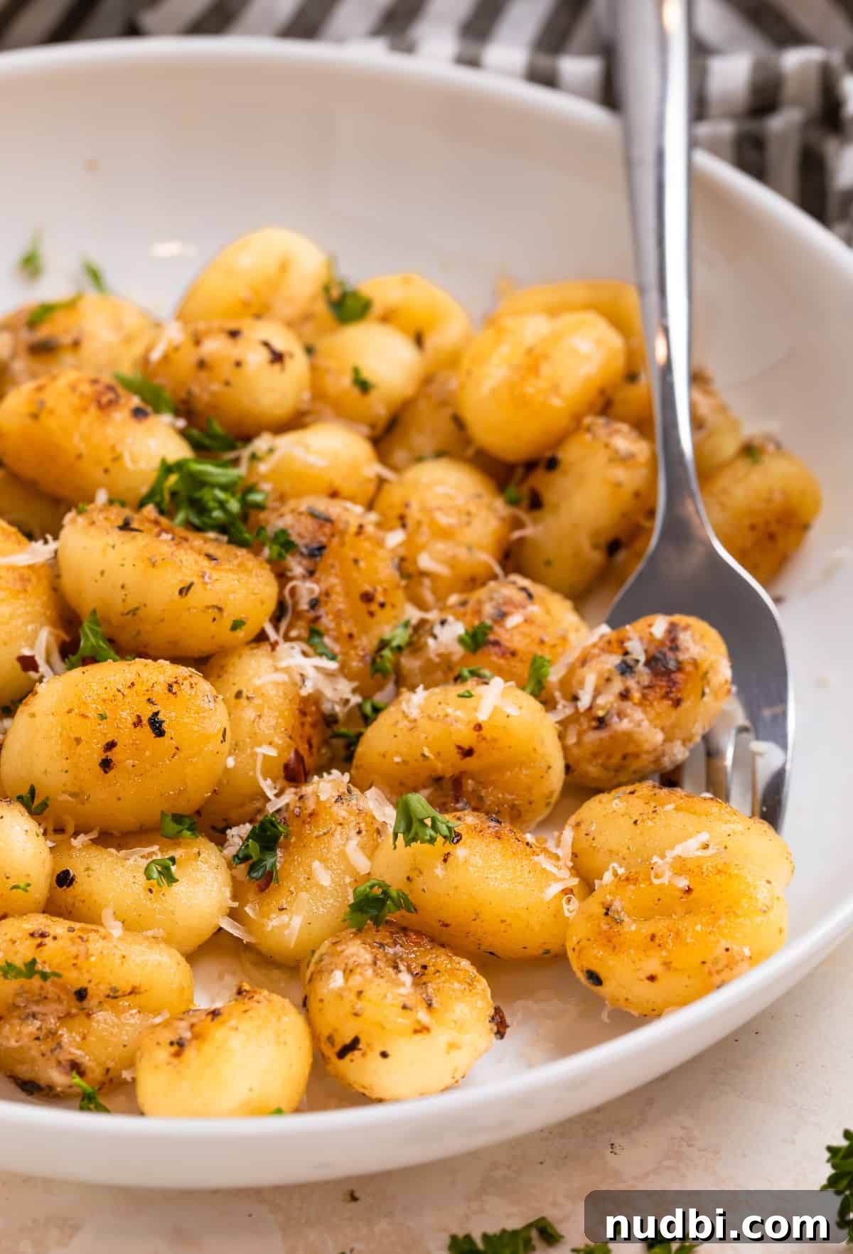 Crispy Pan-Fried Gnocchi with Garlic Butter and Parmesan 11 White plate with fried gnocchi topped with fresh parmesan and parsley.