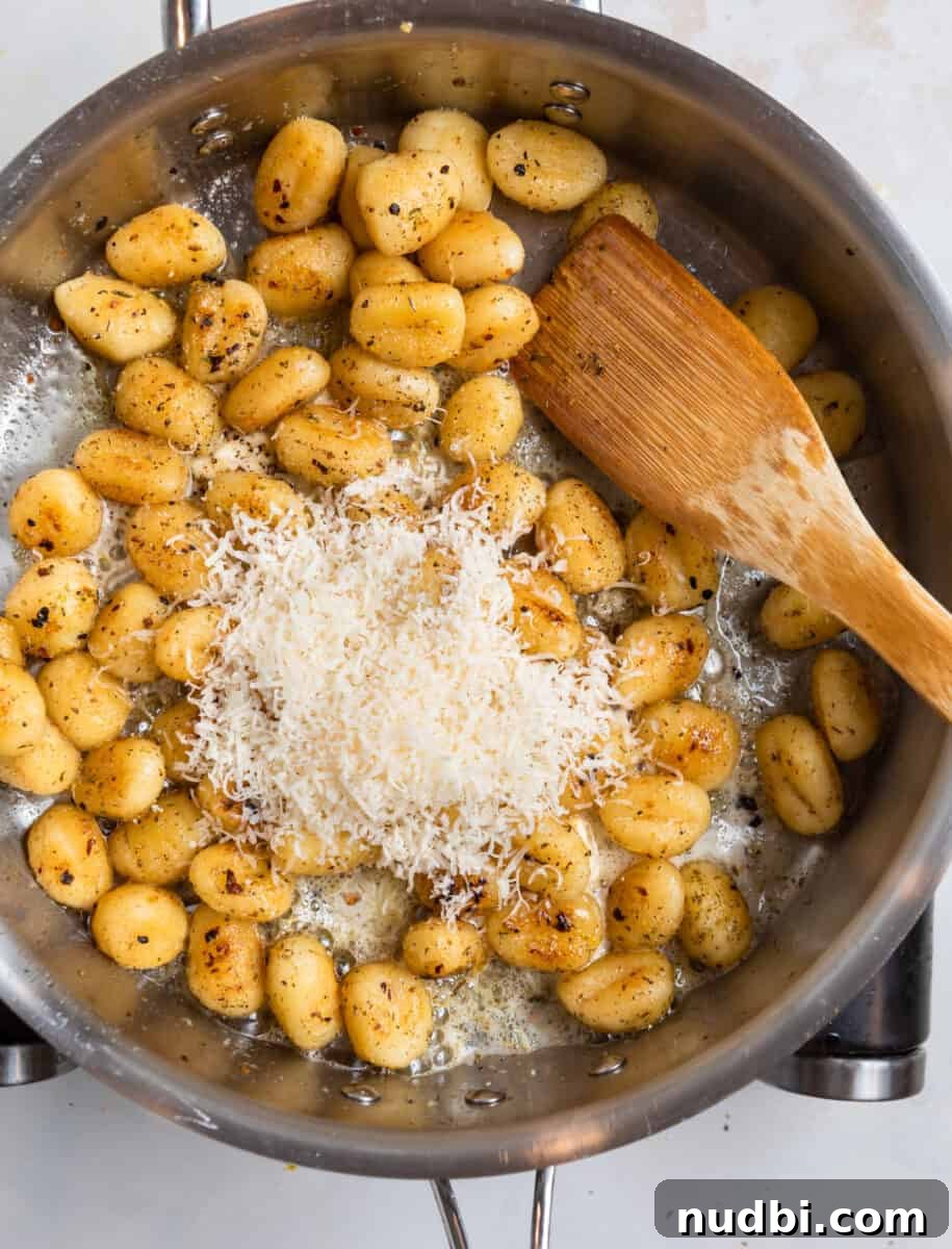 Crispy Pan-Fried Gnocchi with Garlic Butter and Parmesan 8 Parmesan added to skillet with brown wooden spatula.