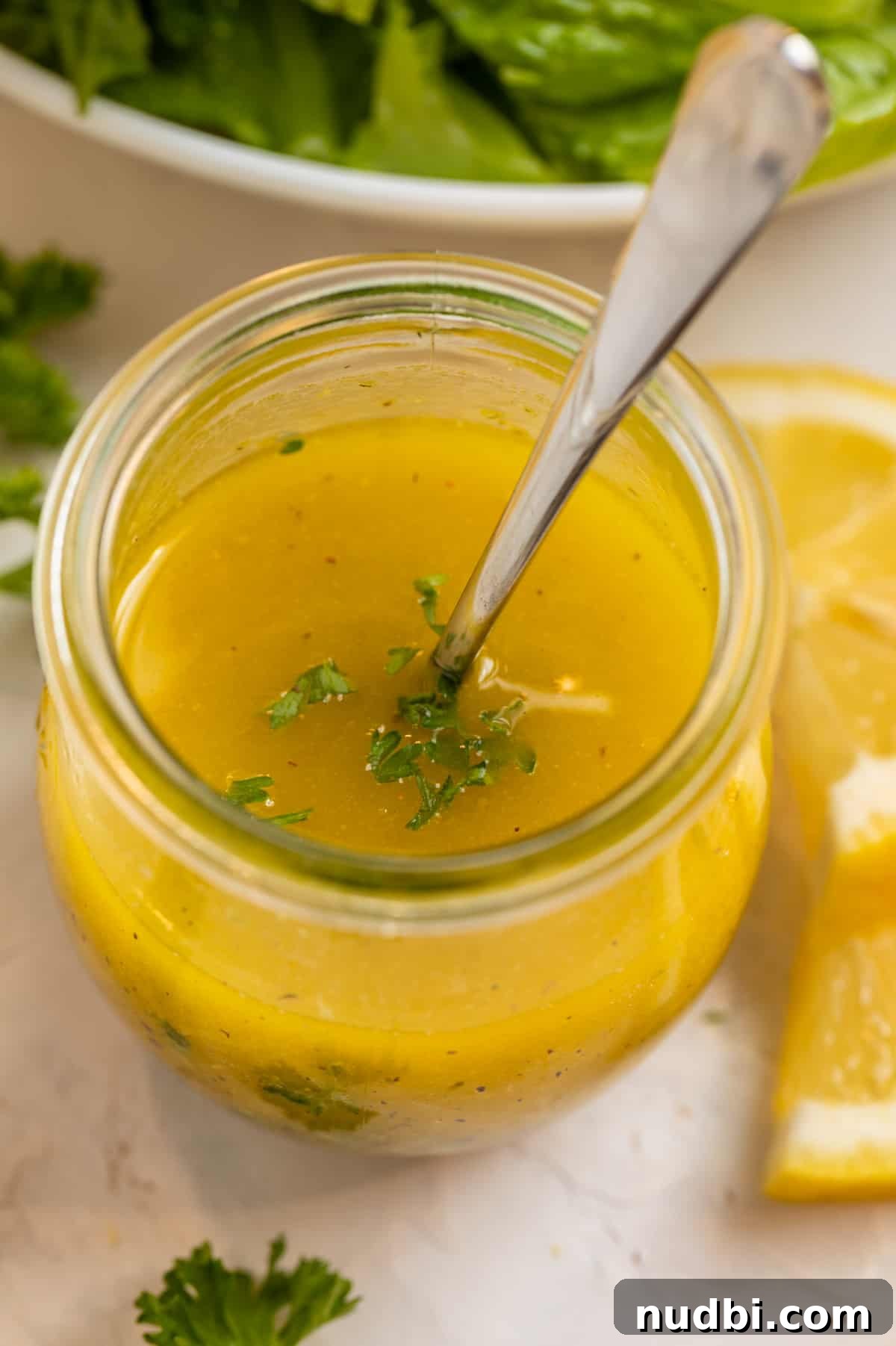 Zesty Lemon Dijon Salad Dressing Recipe 2 Honey lemon dijon dressing in jar topped with chopped parsley and spoon inside.