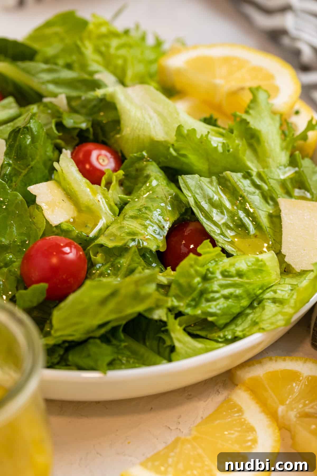 Zesty Lemon Dijon Salad Dressing Recipe 5 White plate with green salad topped with cheese and tomatoes as well as honey lemon dressing.