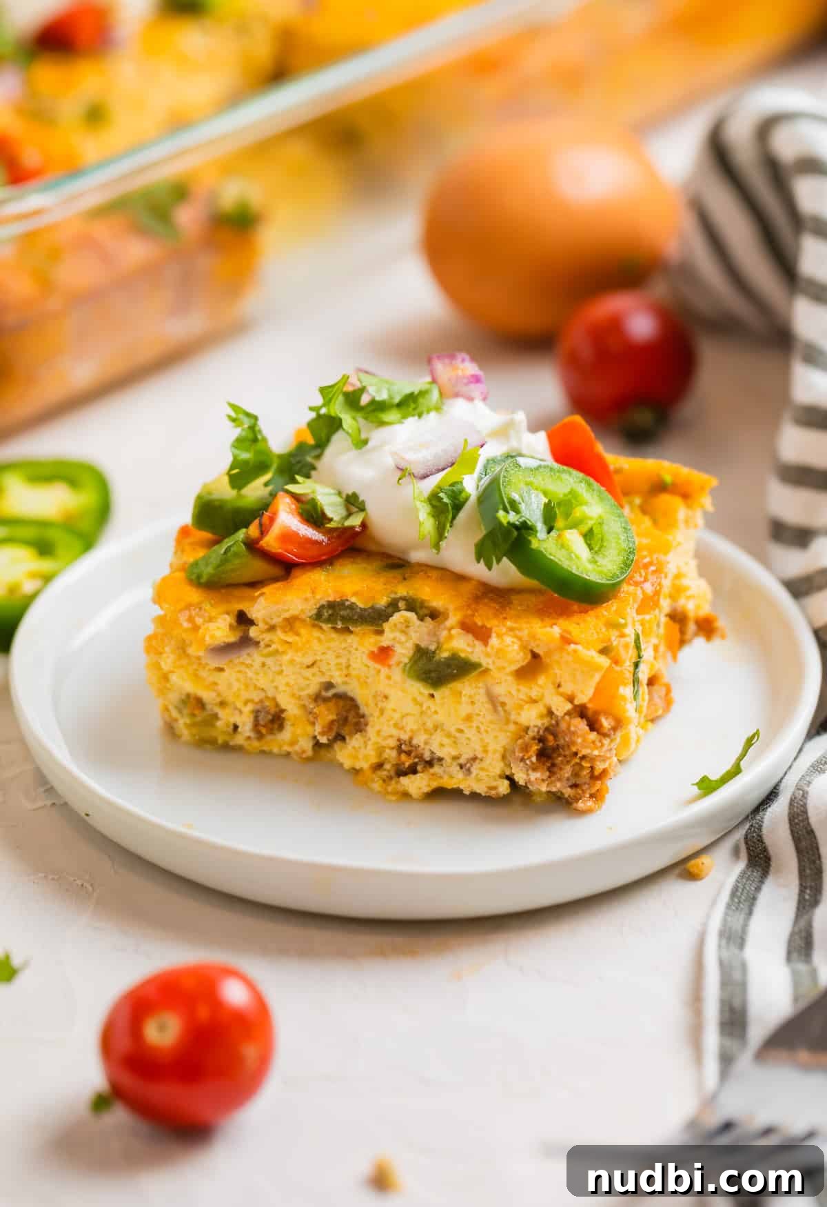 Cheesy Chorizo and Egg Breakfast Casserole 3 Slice of chorizo breakfast casserole topped with sour cream, tomato, cilantro and more on white plate.