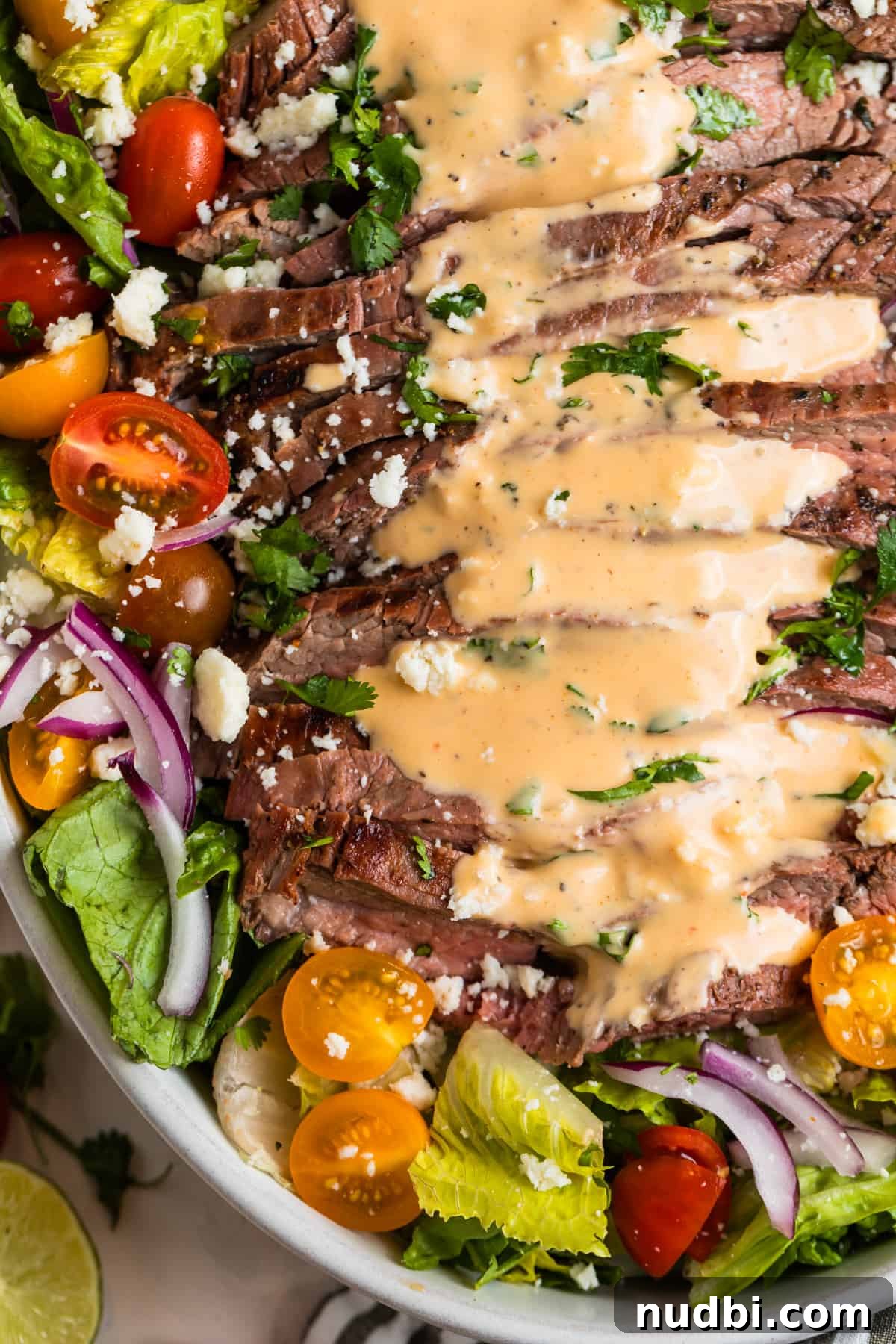 Grilled Flank Steak Salad with Chimichurri and Arugula 3 Grilled flank salad in dish topped with creamy sriracha dressing.