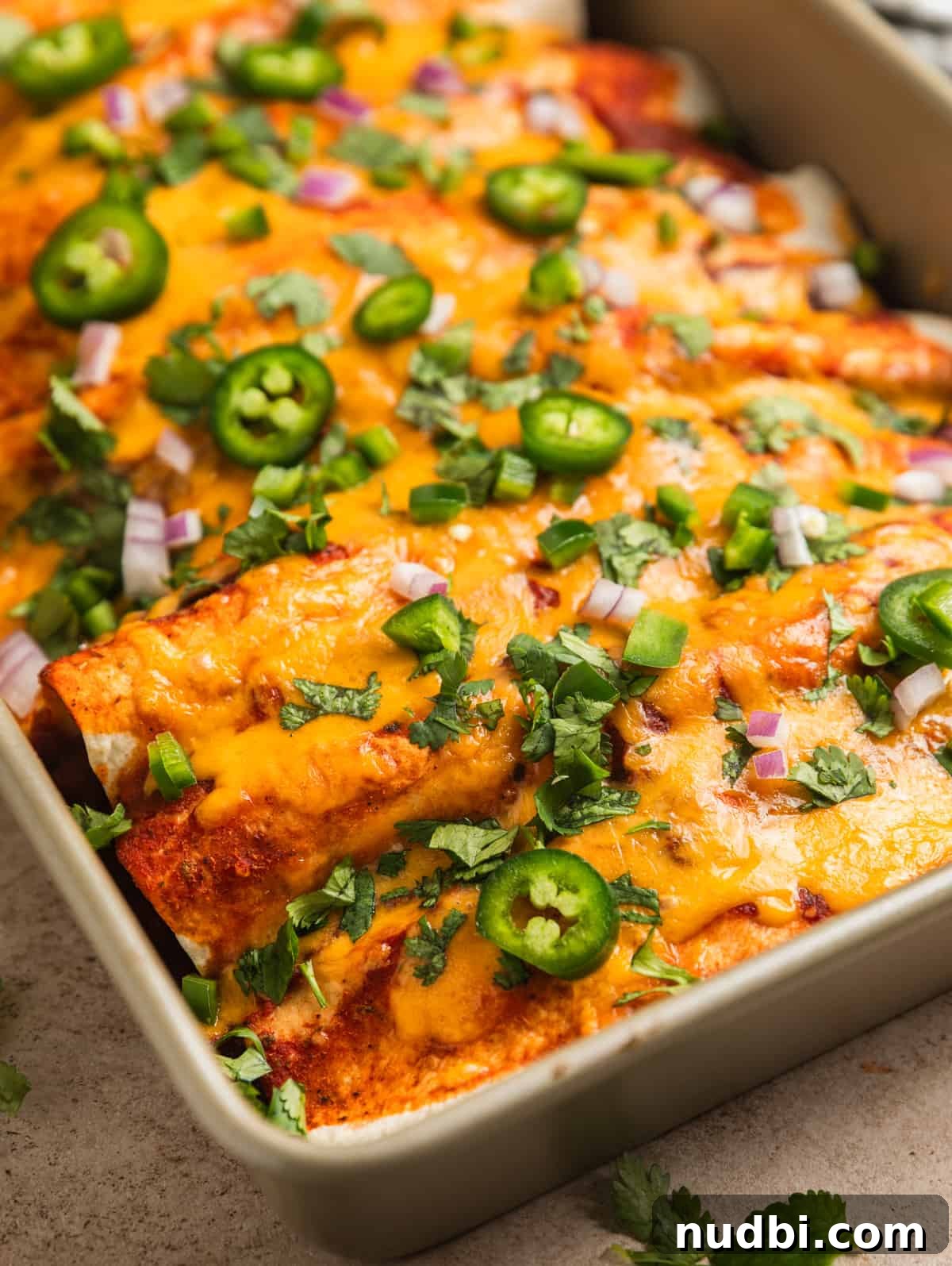 Cheesy Ground Turkey Enchiladas with Homemade Red Sauce 12 Enchiladas in pan topped with melted cheese and other toppings.