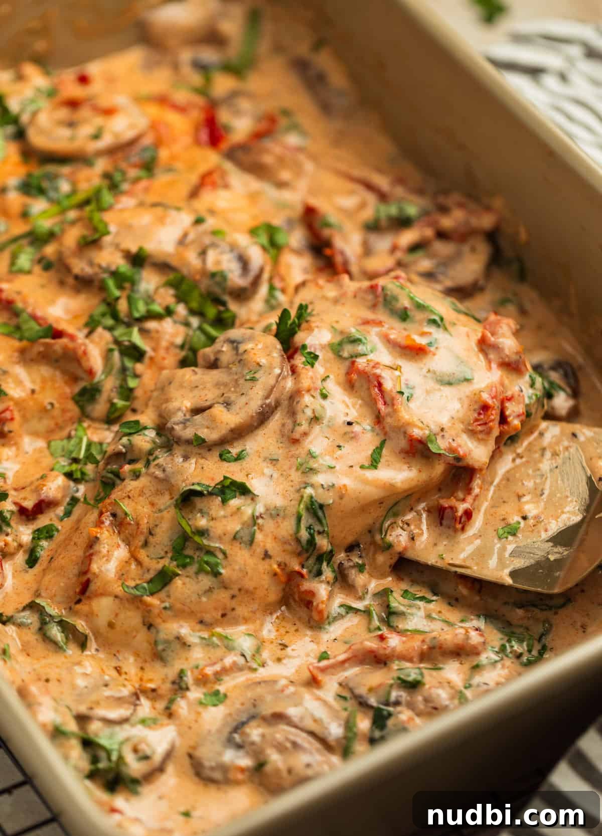 Creamy Baked Tuscan Chicken with Sun-Dried Tomatoes and Spinach 2 Pan with baked tuscan chicken and piece being picked up by spatula.