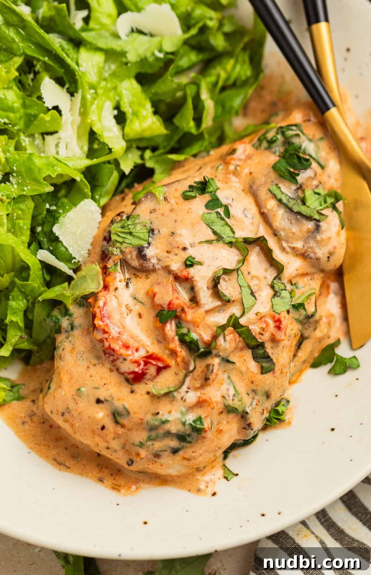 Creamy Baked Tuscan Chicken with Sun-Dried Tomatoes and Spinach 11 Creamy baked Tuscan chicken breast on white plate with salad and fork.