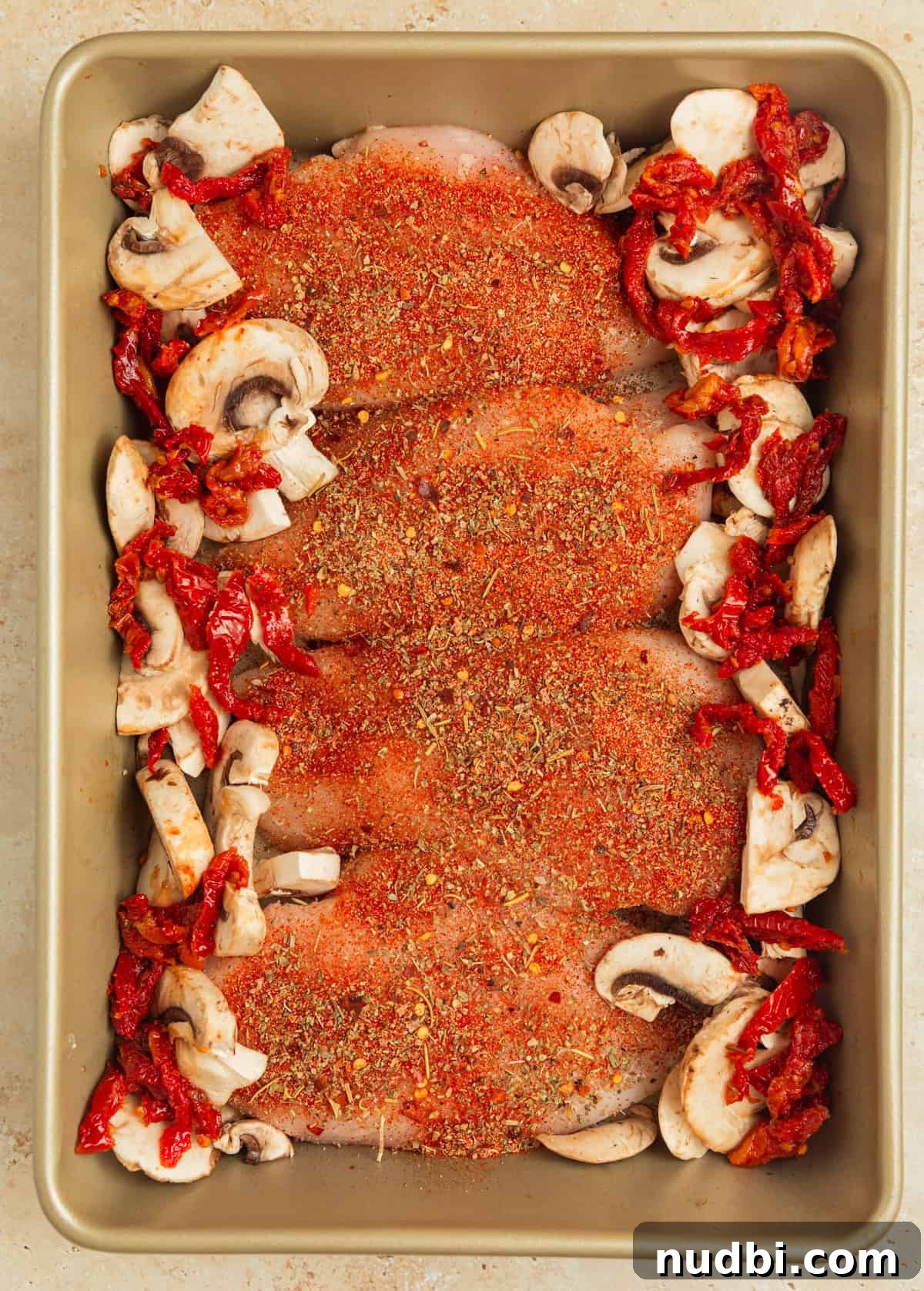 Creamy Baked Tuscan Chicken with Sun-Dried Tomatoes and Spinach 5 Baking pan with seasoned chicken with mushrooms and sun-dried tomatoes lining the edges of the pan.