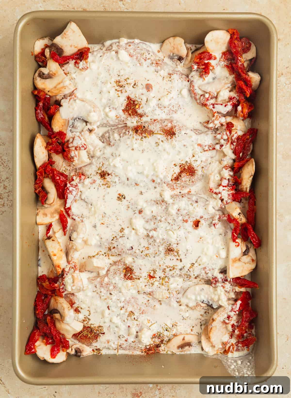 Creamy Baked Tuscan Chicken with Sun-Dried Tomatoes and Spinach 8 Cream sauce poured over seasoned chicken in pan before baking.