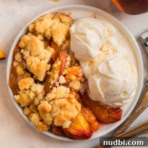 Peach Cobbler Made with Cake Mix: Quick Southern Dessert recipe 11 Overhead view of peach cobbler with cake mix on white plate with two scoops of vanilla ice cream.