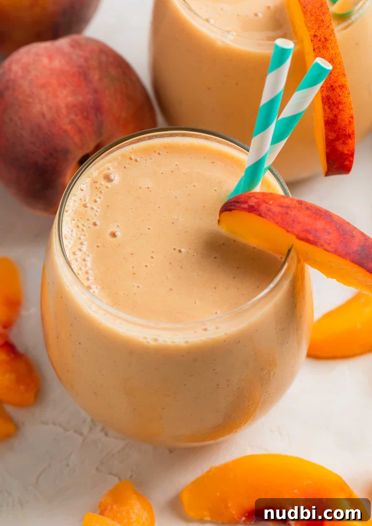 Creamy Banana and Peach Smoothie Recipe for Summer Refreshment 2 Peach banana smoothie in glass with two straws and peach slice garnish.