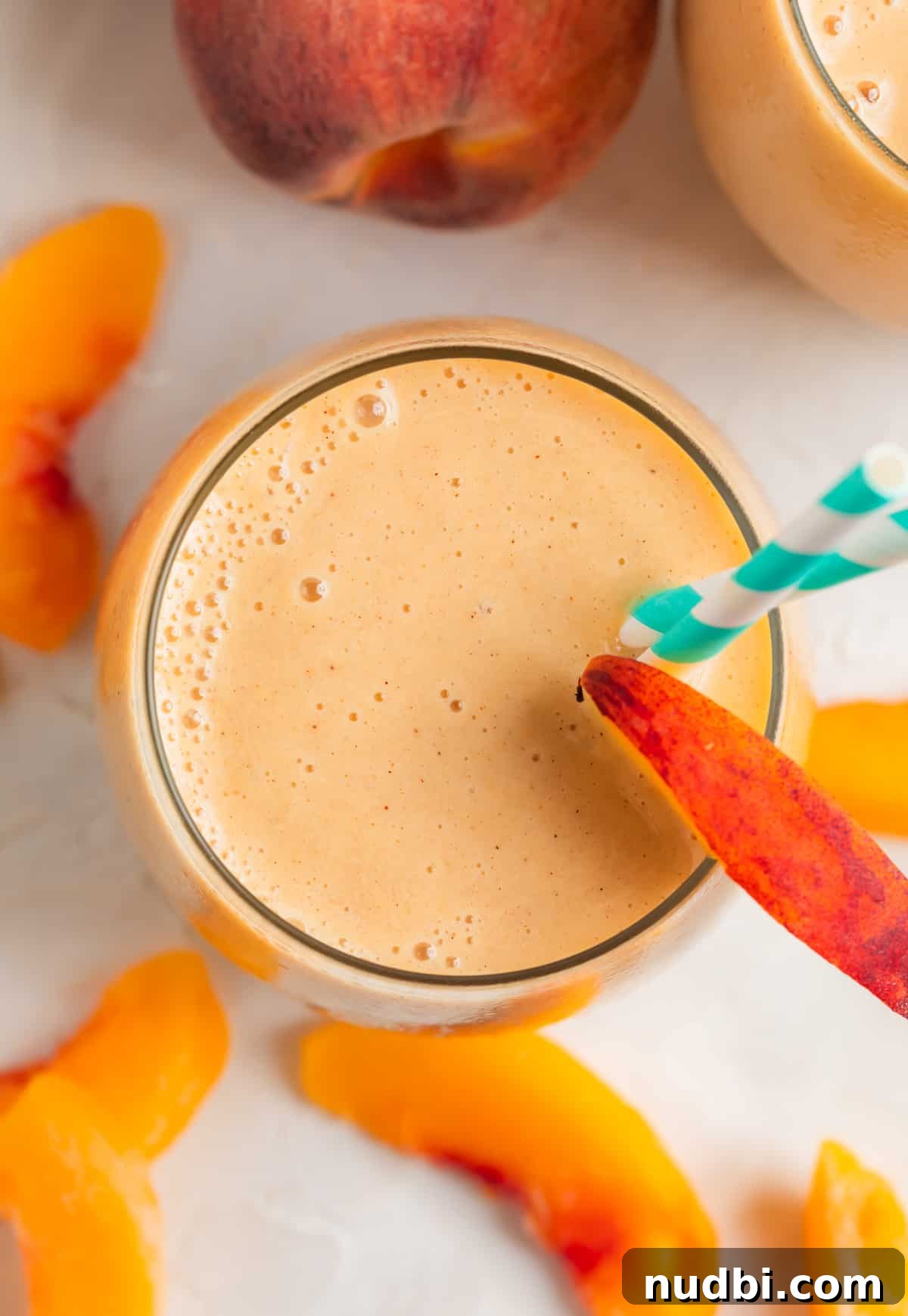 Creamy Banana and Peach Smoothie Recipe for Summer Refreshment 5 Peach and banana smoothie with peach slice garnish in glass cup with teal and white striped straw.