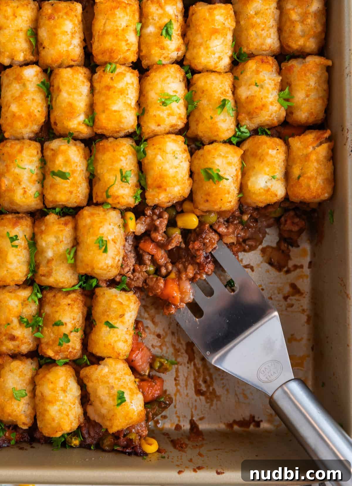 Tater Tot Shepherd’s Pie Recipe: Comforting Family Meal 2 Shepherd's pie topped with tater tots in pan with spatula scooping out serving.