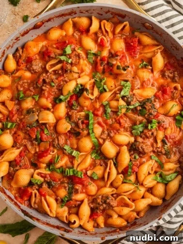 Ground beef pasta in skillet topped with basil.