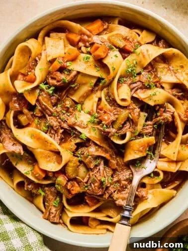 Bowl with short rib ragu tossed with pasta and chopped fresh parsley over top.
