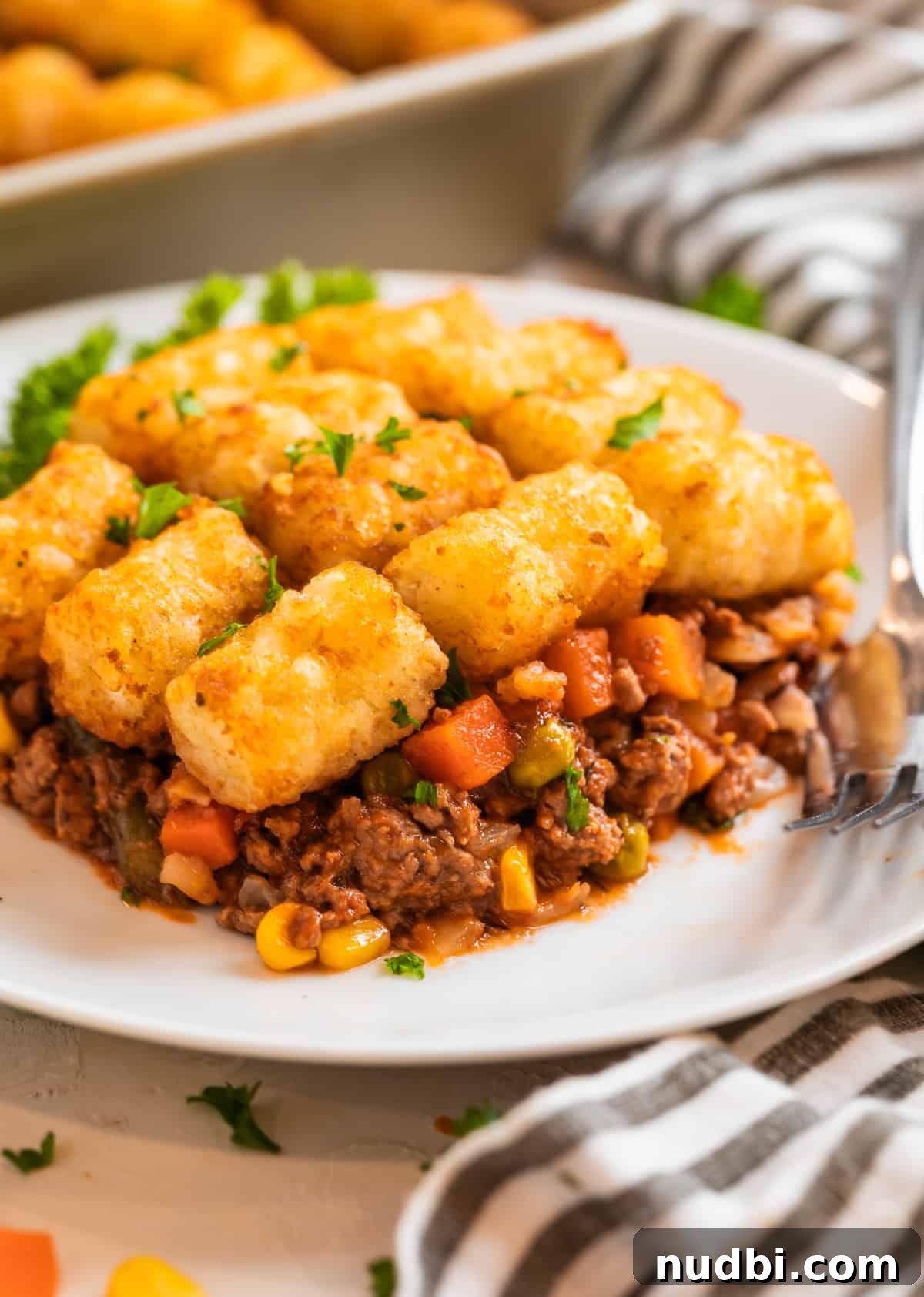 Tater Tot Shepherd’s Pie Recipe: Comforting Family Meal 3 Tater tot shepherd's pie on white plate with fork and topped with chopped parsley.