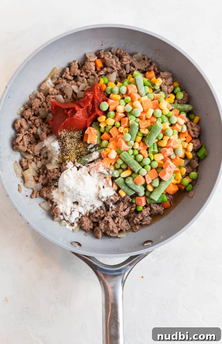 Tater Tot Shepherd’s Pie Recipe: Comforting Family Meal 5 Frozen mixed vegetables, beef, tomato paste, corn starch and other ingredients in skillet.