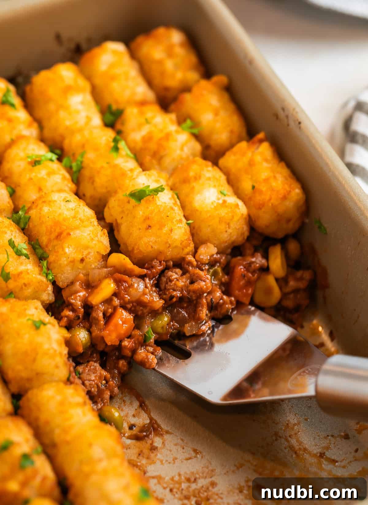Tater Tot Shepherd’s Pie Recipe: Comforting Family Meal 10 Tater tot topped beef mixture in baking pan with spatula scooping into the dish.