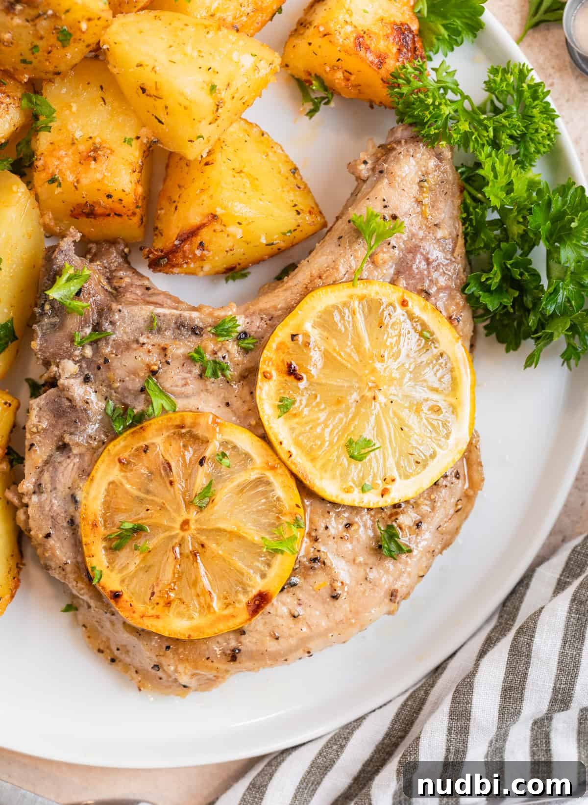 Crispy Lemon Pepper Pork Chops with Garlic Butter Sauce 2 Lemon pepper pork chop on white plate with parsley and potatoes.
