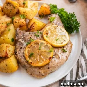 Crispy Lemon Pepper Pork Chops with Garlic Butter Sauce 10 Lemon pepper pork chop on white plate with lemon slices and freshly chopped parsley.