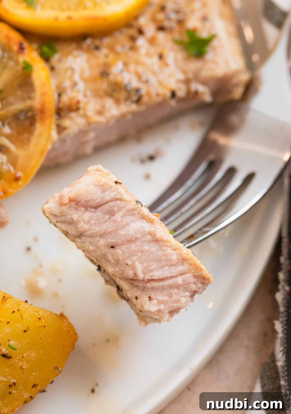 Crispy Lemon Pepper Pork Chops with Garlic Butter Sauce 3 White plate with piece of lemon pepper pork chop on fork.